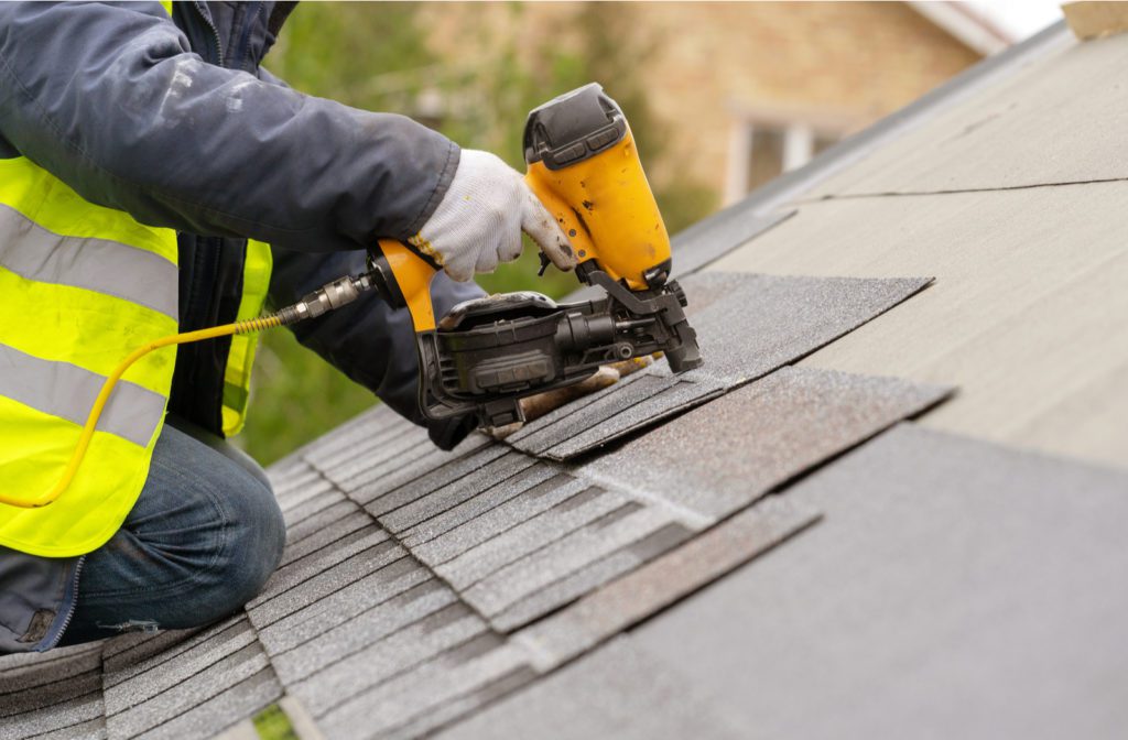 Professional with safety vest, gloves and pneumatic nail gun installing new roof on house