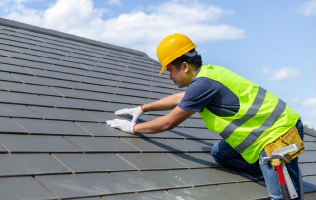 Man on top of roof working on roof maintenance while wearing safety equipment