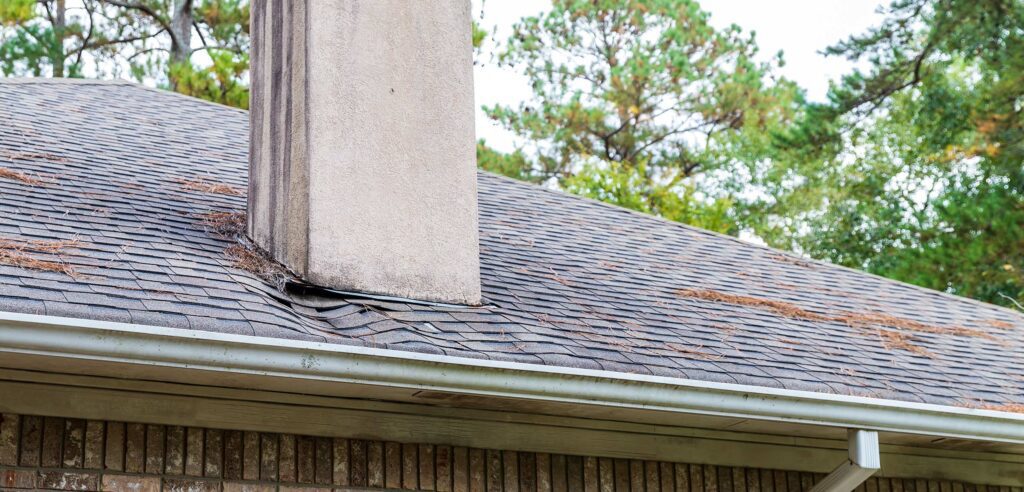 Sagging shingles near chimney on roof.