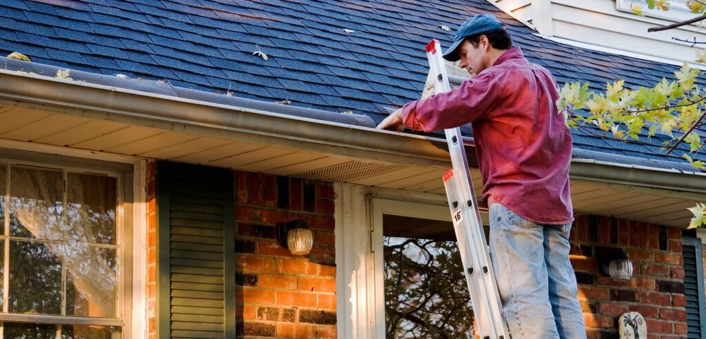 Man on ladder cleans gutters by hand.