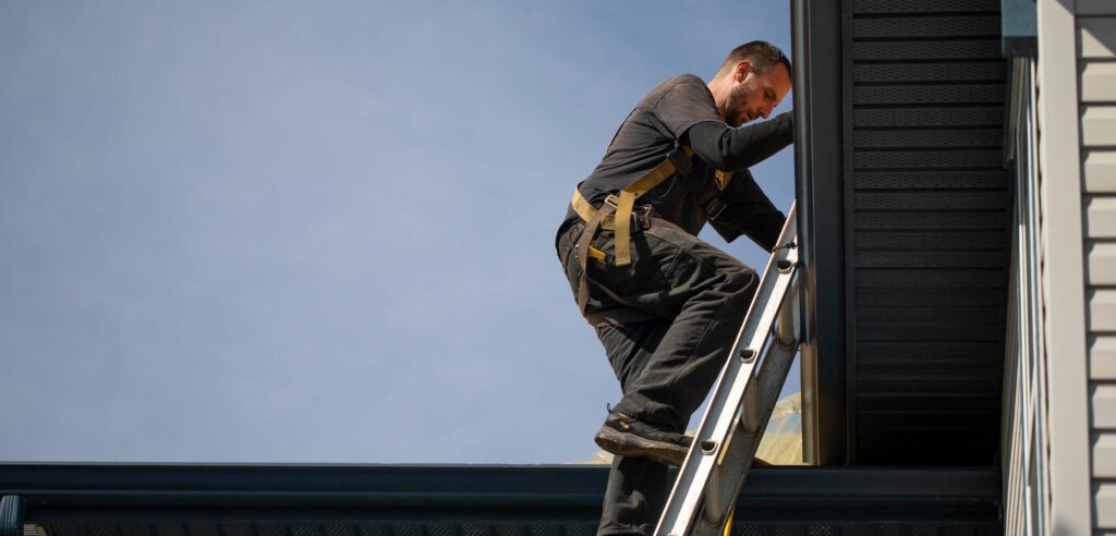 Worker on ladder cleans gutters.