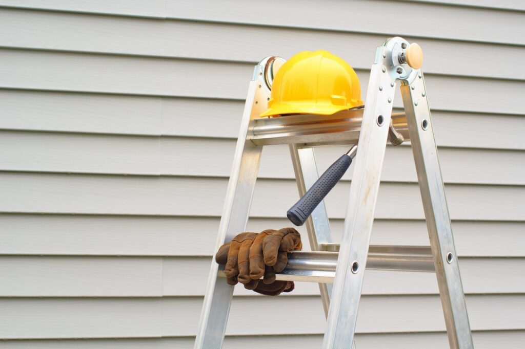 Stepladder, hardhat, gloves and hammer with house siding background