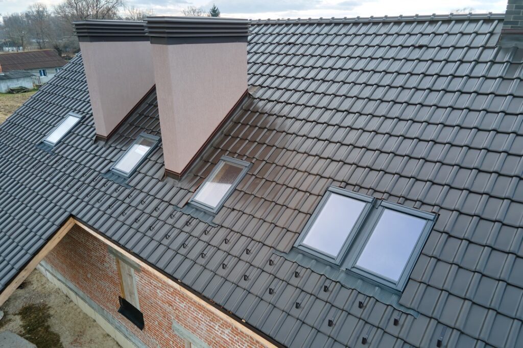 Closeup of attic windows and brick chimneys on house roof top covered with ceramic shingles. Tiled covering of building.