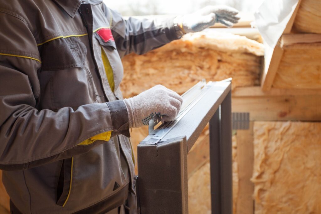 Concept of building process. Cropped view of professional workman standing in new house under construction with new metallic skylight window frame for mansard room