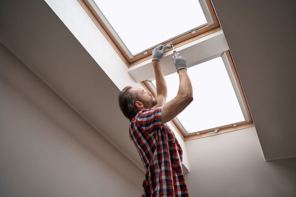 Young caucasian worker screwing skylight window handle holding screwdriver in right hand. Home master concept, construction and repair