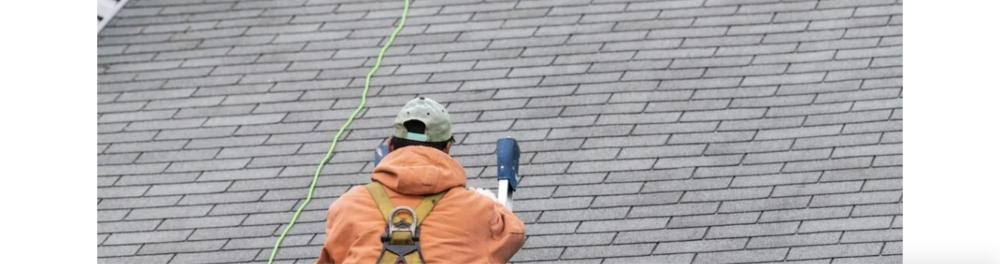 A Guns N Hoses roofing technician in full safety gear, carefully inspects a residential roof after service.