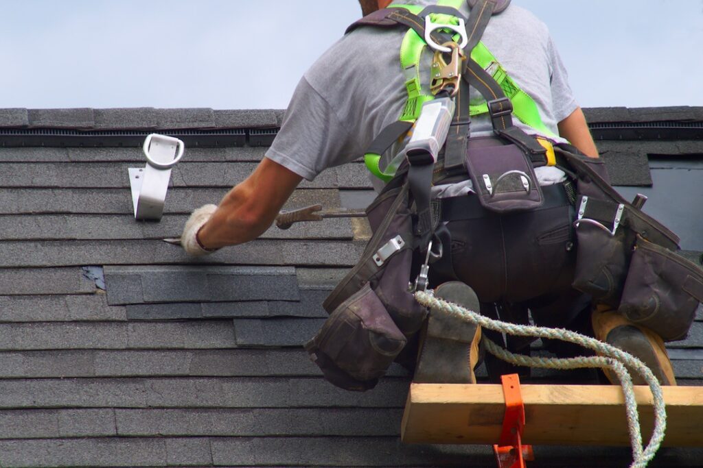 Professional roofing contractor using all required safety equipment to work on roof at angle