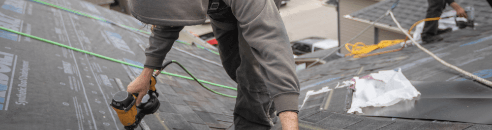 A roofer carefully nails down the first layer of roofing material.