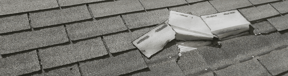 Lifted and damaged shingles post-storm, exposing the underlayer of a roof.