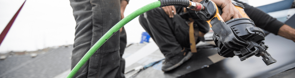 A close up image of a nail gun as it nails in new shingles.