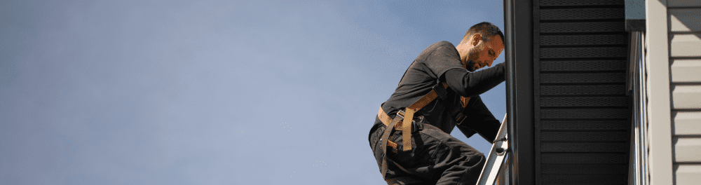 A Guns N Hoses gutter technician carefully climbs a ladder so he can get a better view of a home's gutter system.