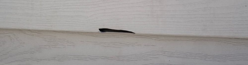 A close up image of vinyl siding showing a hole.
